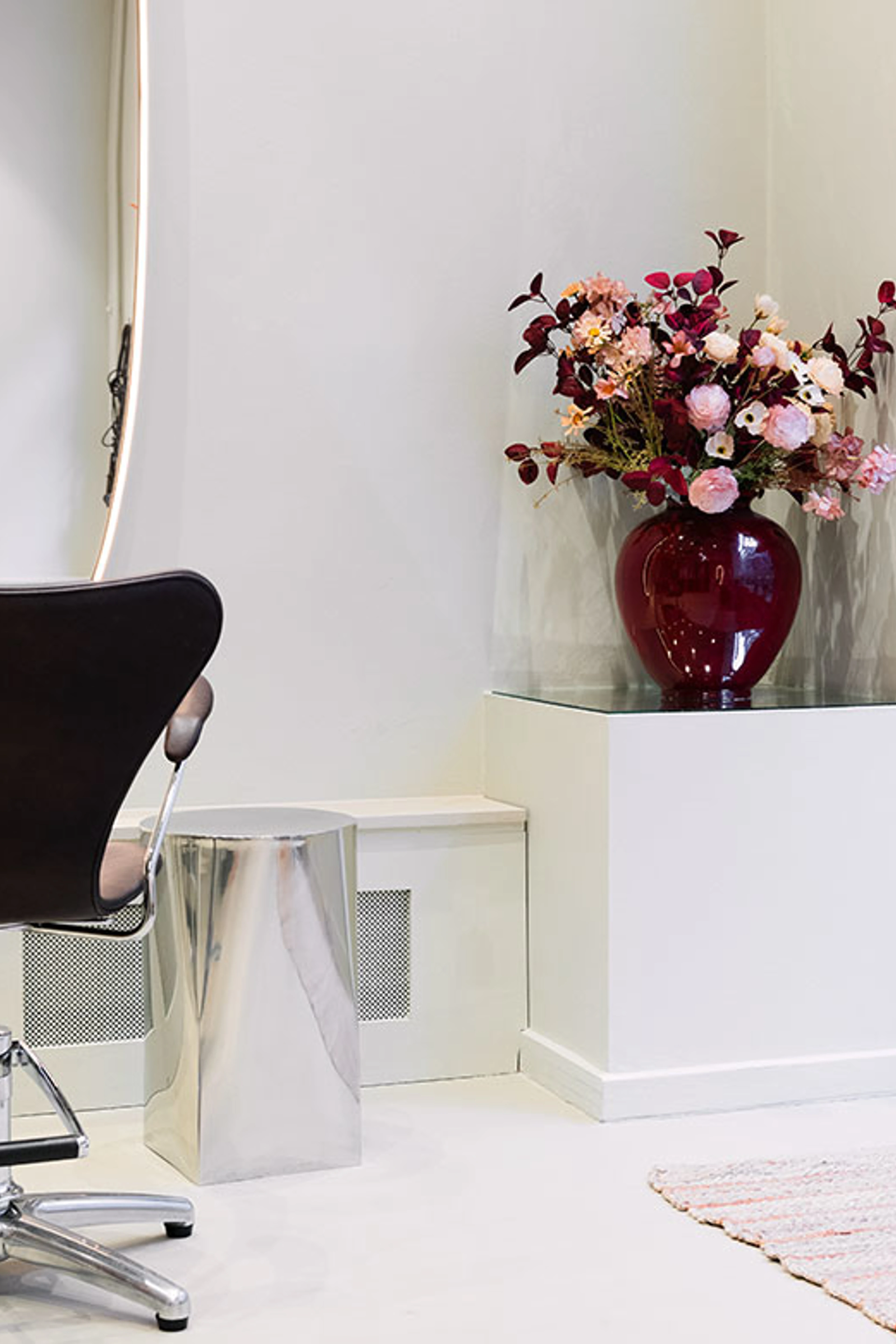 Rød vase med blomster på piedestal ved frisørplads i lys salon.
