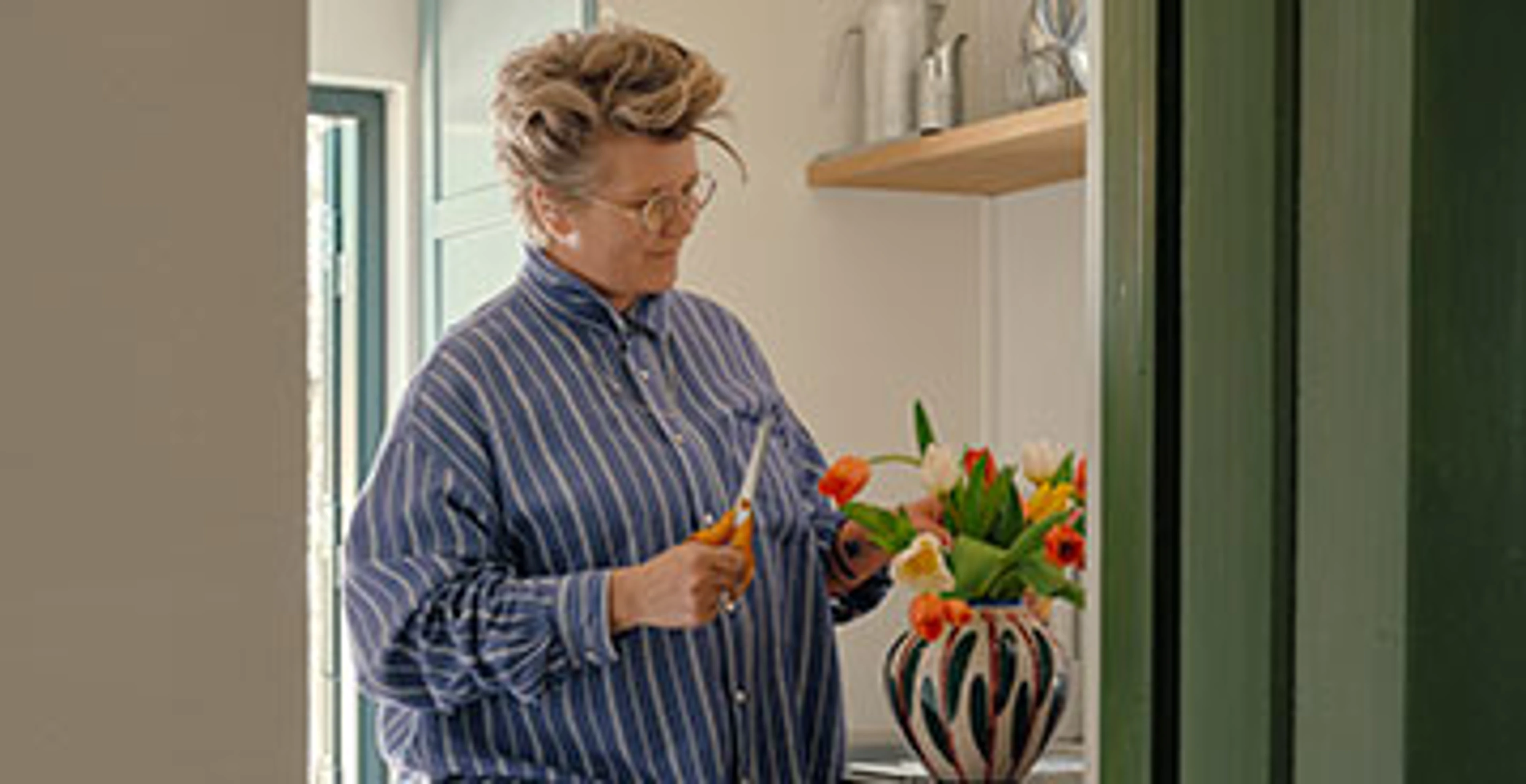 Carla står og arrangerer en buket tulipaner i lyst køkken.
