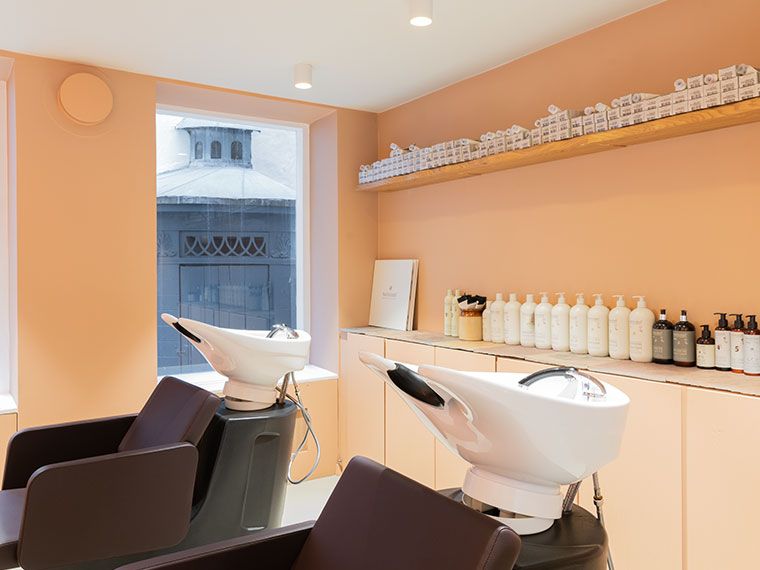 Frisørsalon med to hårvaske, lyse vægge og hylder med hårplejeprodukter.