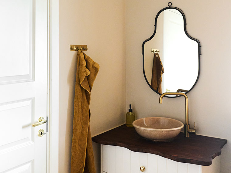 Bathroom with a light beige wall, organically shaped black-framed mirror, bowl-shaped sink, and brass faucet.