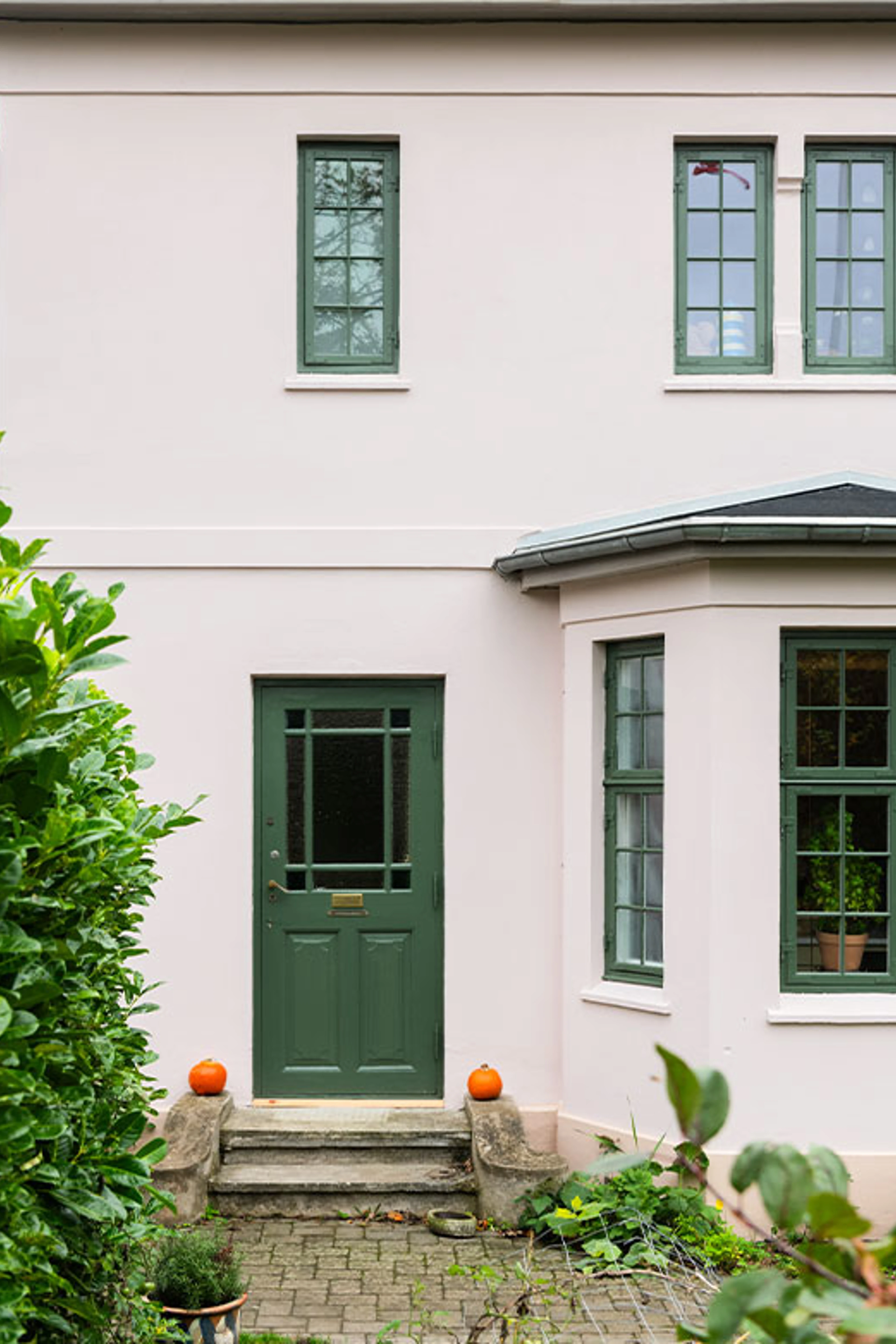 Lys husfacade med grøn hoveddør, vinduer og lille forhave.