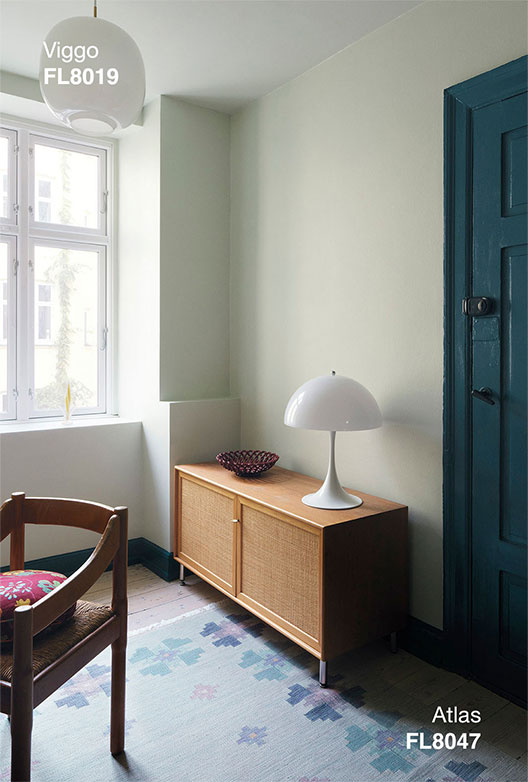 Rum med vægge i Viggo og dør i Atlas, indrettet med skænk i træ, bordlampe og stol ved vinduet.