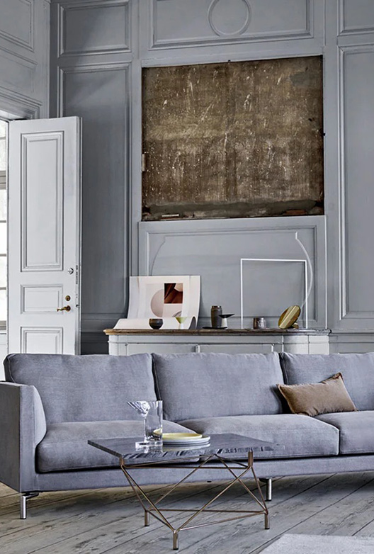 Stue med grå vægge, en grå sofa, og et stuebord med stenplade og metalben. Bagved sofaen er der en stor sten indfattet i væggen.