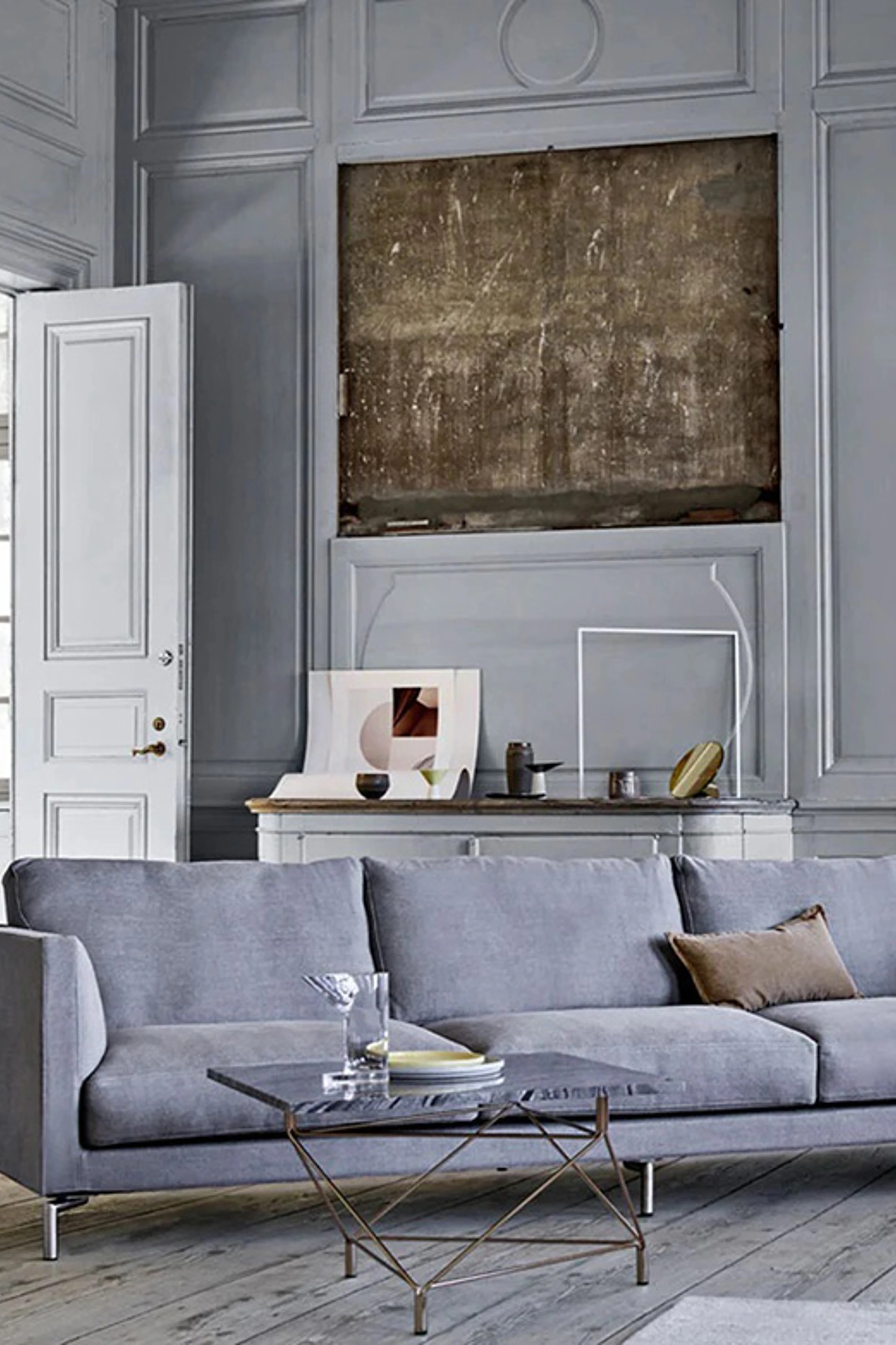 Stue med grå vægge, en grå sofa, og et stuebord med stenplade og metalben. Bagved sofaen er der en stor sten indfattet i væggen.