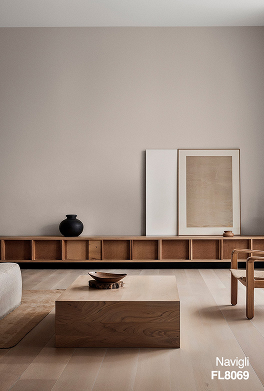 Minimalistiskt vardagsrum med väggar målade i den varma greige färgen Navigli FL8069. Ljusa trägolv, en låg trähylla, soffbord i massivt trä och enkla dekorativa element ger rummet ett lugnt och tidlöst uttryck.