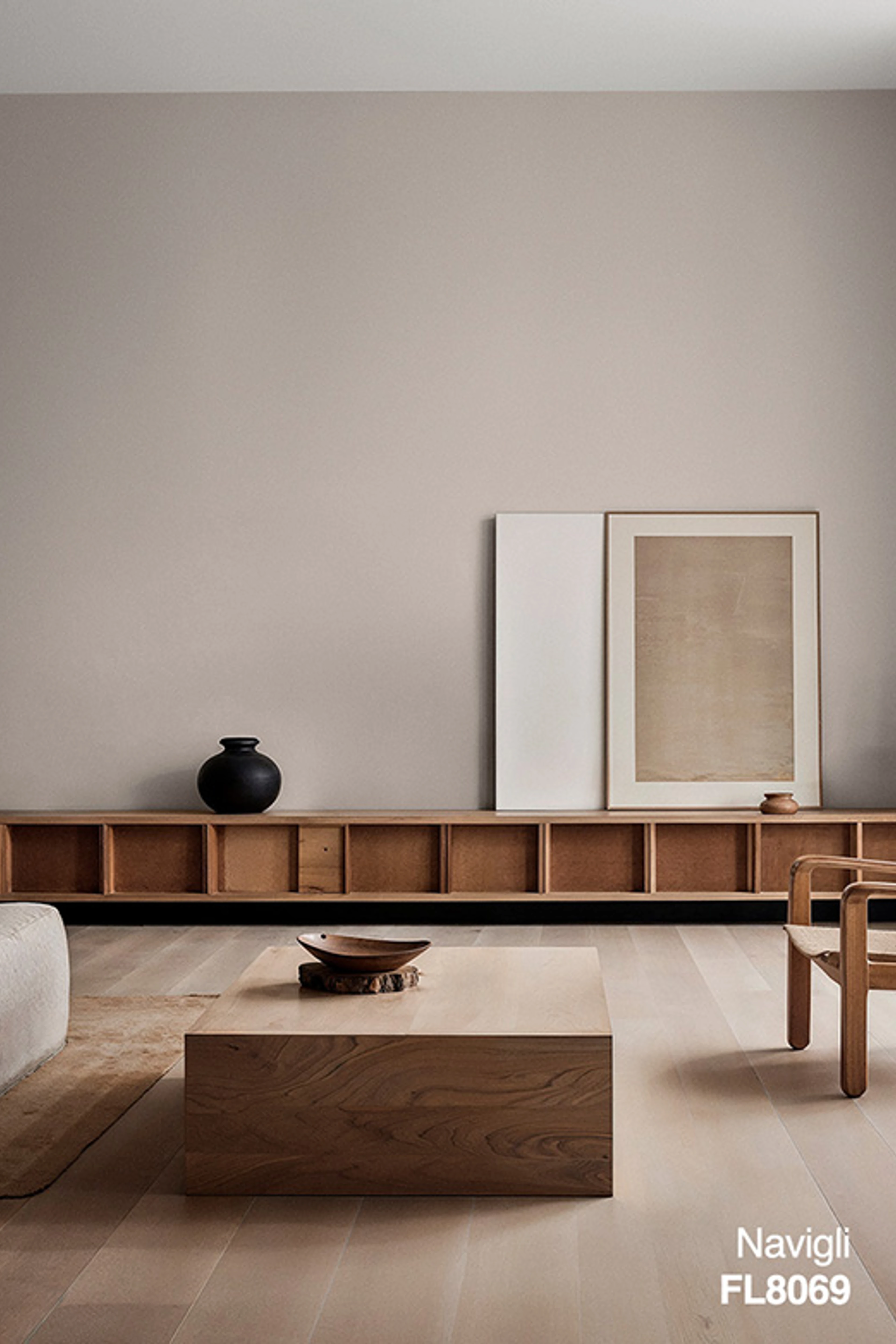 Minimalistiskt vardagsrum med väggar målade i den varma greige färgen Navigli FL8069. Ljusa trägolv, en låg trähylla, soffbord i massivt trä och enkla dekorativa element ger rummet ett lugnt och tidlöst uttryck.