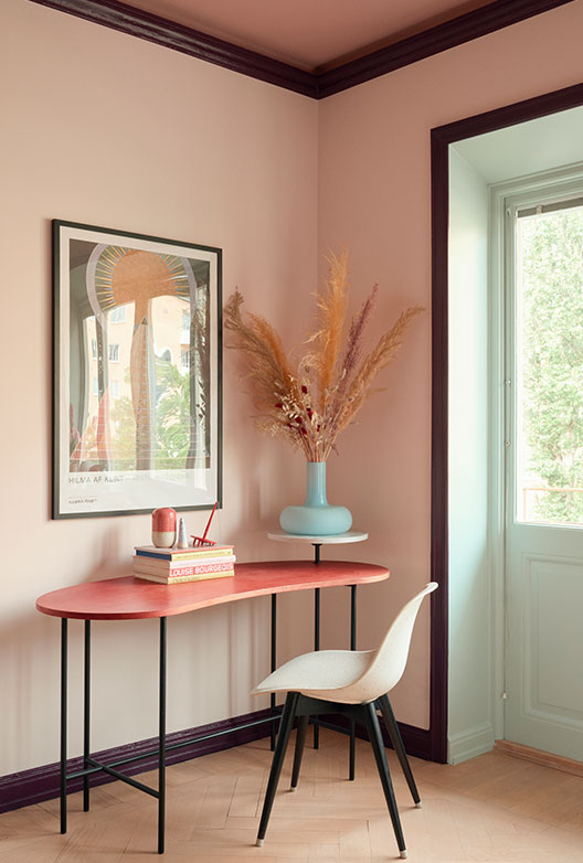 Lille arbejdsplads med rosa vægge og rødt bord.