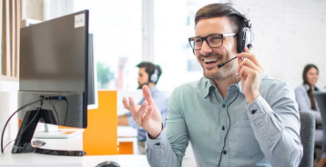 Medarbejder med headset taler i telefon ved en computer på et kontor.