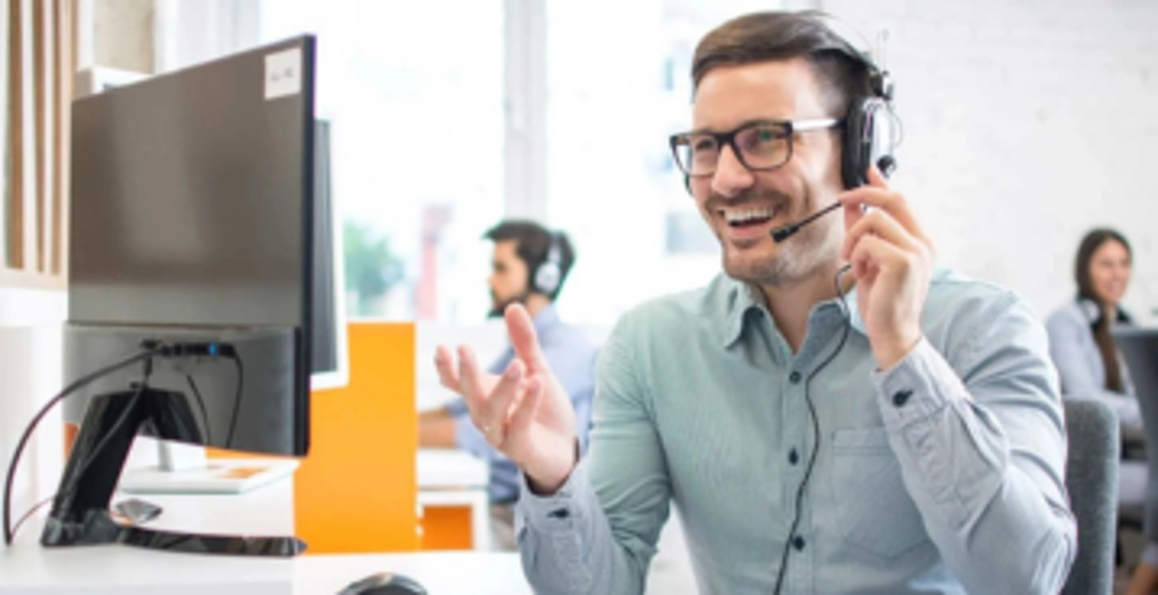 Medarbejder med headset taler i telefon ved en computer på et kontor.