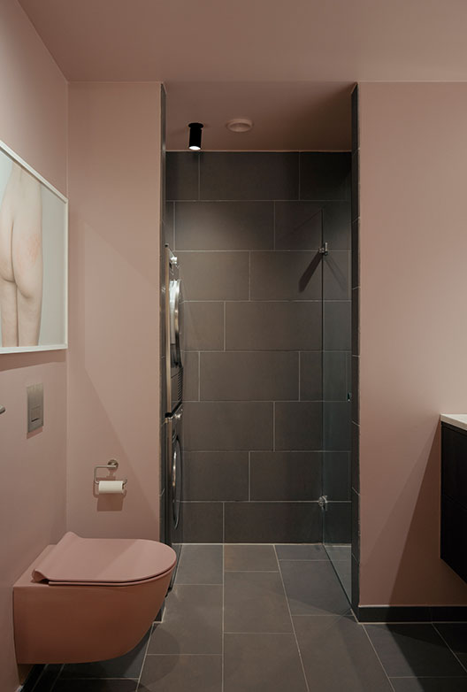 Badeværelse med rosa vægge, bruseniche og væghængt toilet.