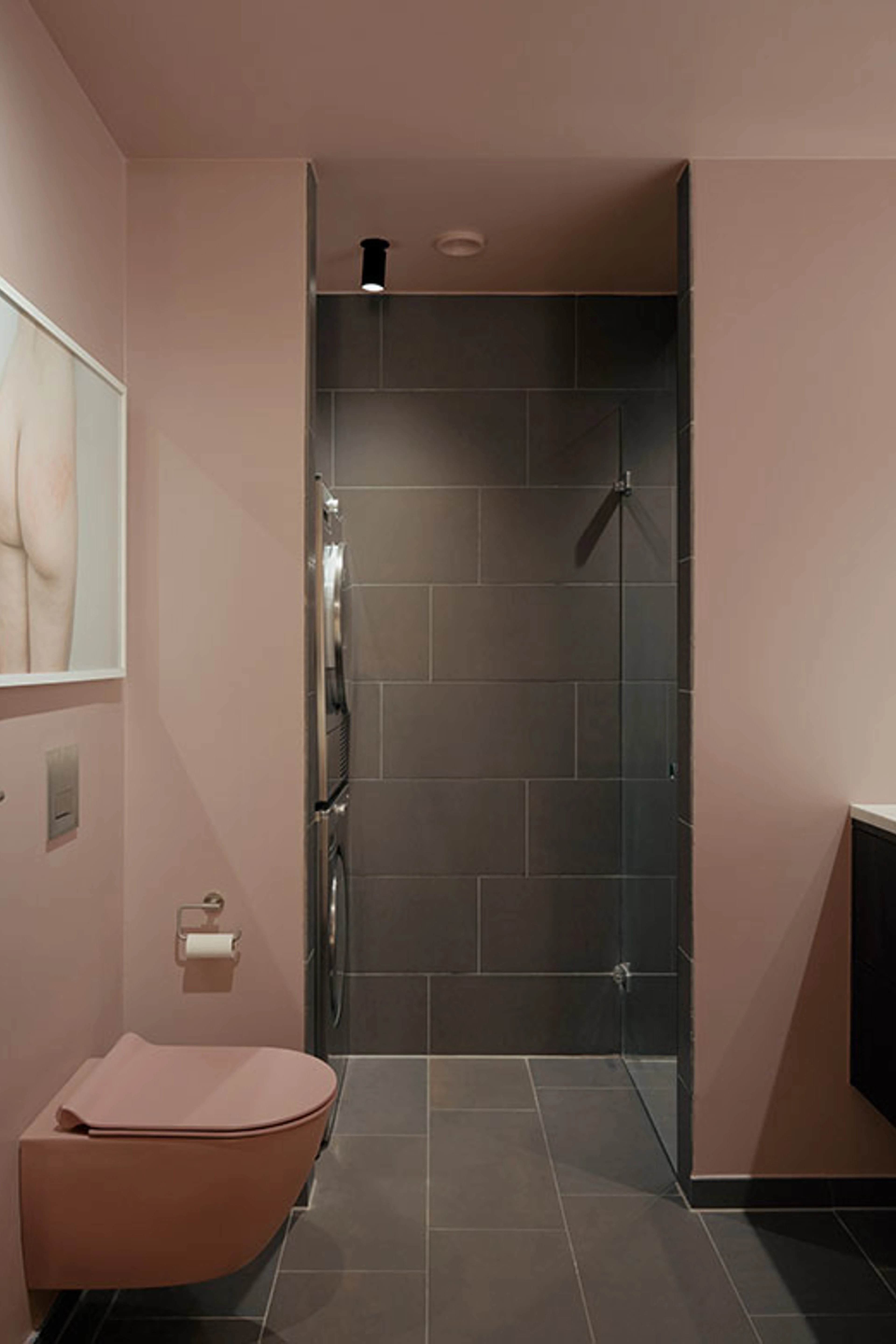 Badeværelse med rosa vægge, bruseniche og væghængt toilet.