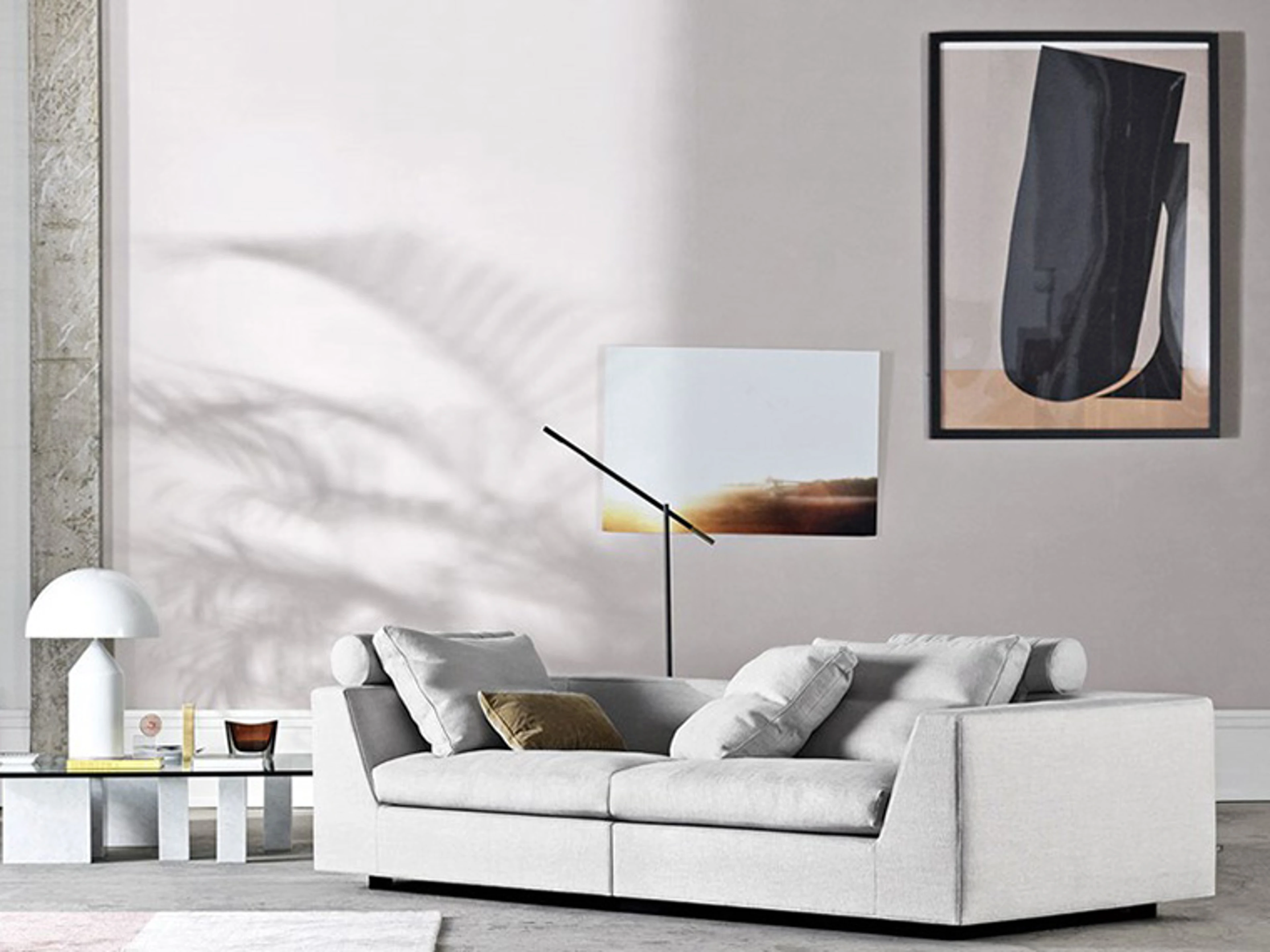 Stue med hvitlige vegger, en lysegrå sofa og et sofabord med glassplate og marmorben. Det er en hvit lampe med skjerm på sofabordet. På veggen er det et maleri.