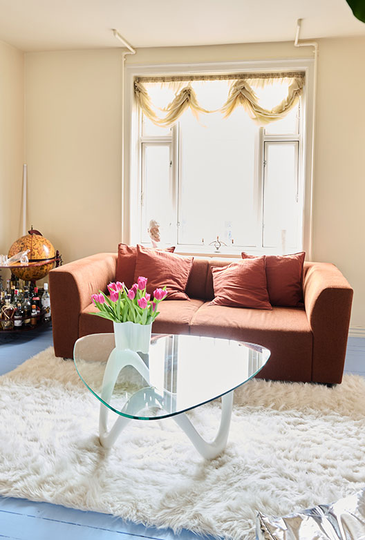 Stue med brun sofa, glasbord, tulipaner og stort vindue.