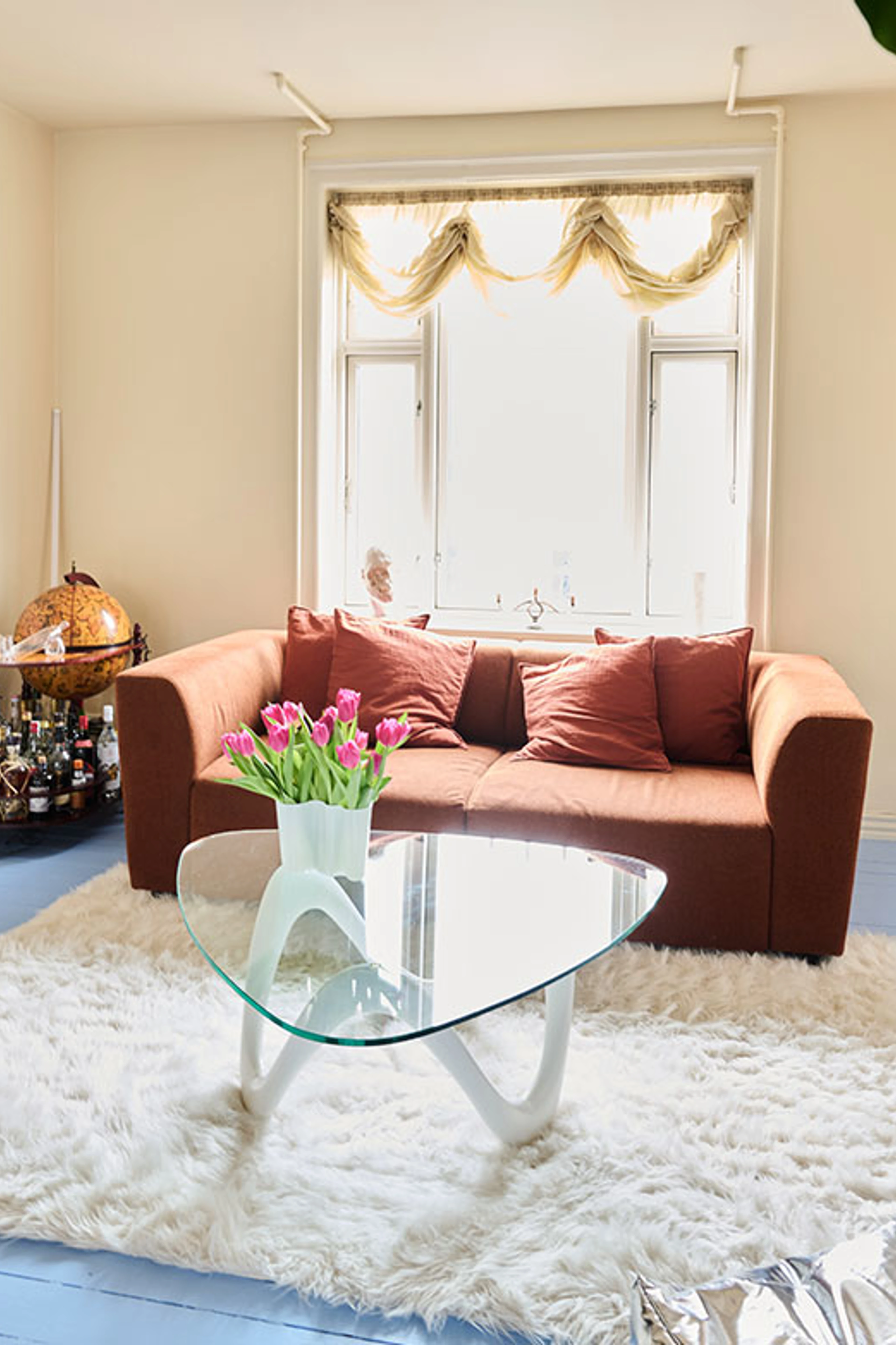 Stue med brun sofa, glasbord, tulipaner og stort vindue.