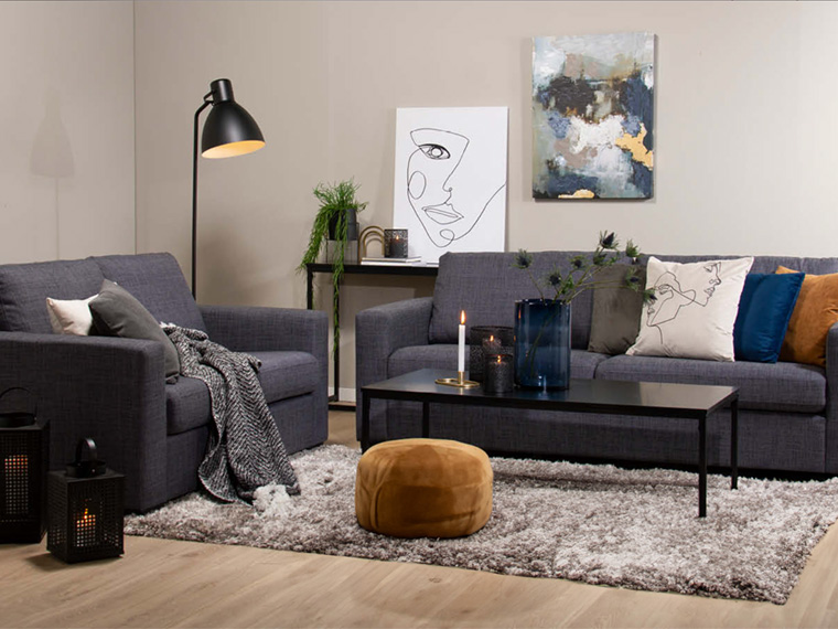 Stue med beige vegger, grå sofaer, svart sofabord og dekorativ veggkunst.