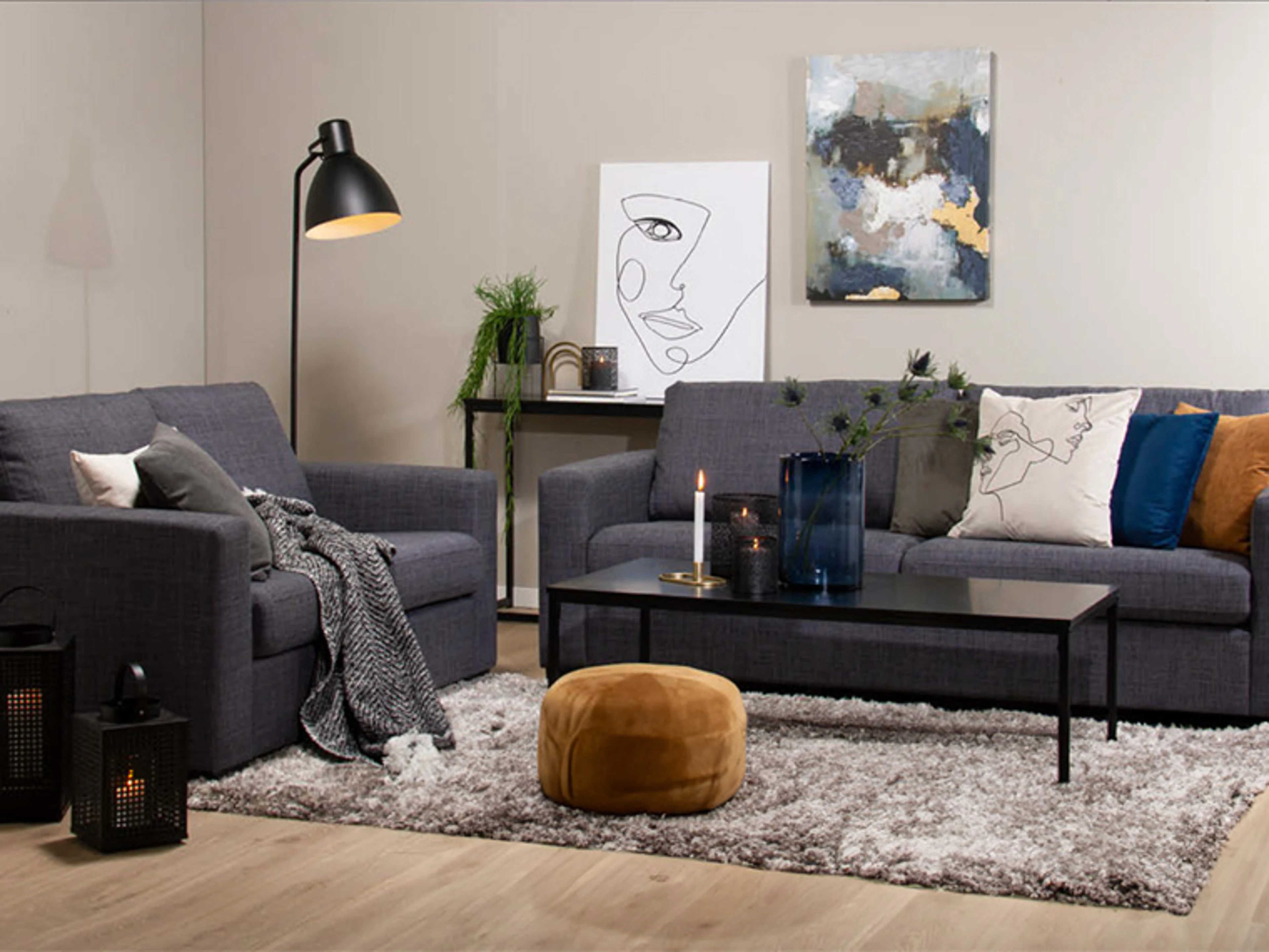 Stue med beige vegger, grå sofaer, svart sofabord og dekorativ veggkunst.