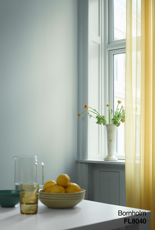 Ljust matplats med ljusgrå väggar, gula genomskinliga gardiner, vitt fönster och bord med citroner, glas och vas med blommor.