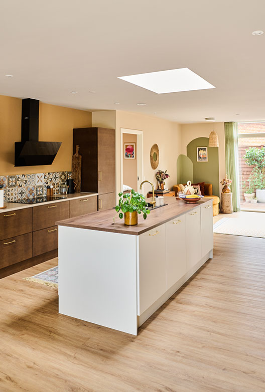 Open-plan kitchen and living area with warm beige walls, wood cabinetry, a white kitchen island, and decorative patterned tiles.