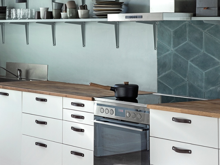 Modern kitchen with light blue walls, white cabinets, wooden worktops, open shelving and geometric blue wall tiles.
