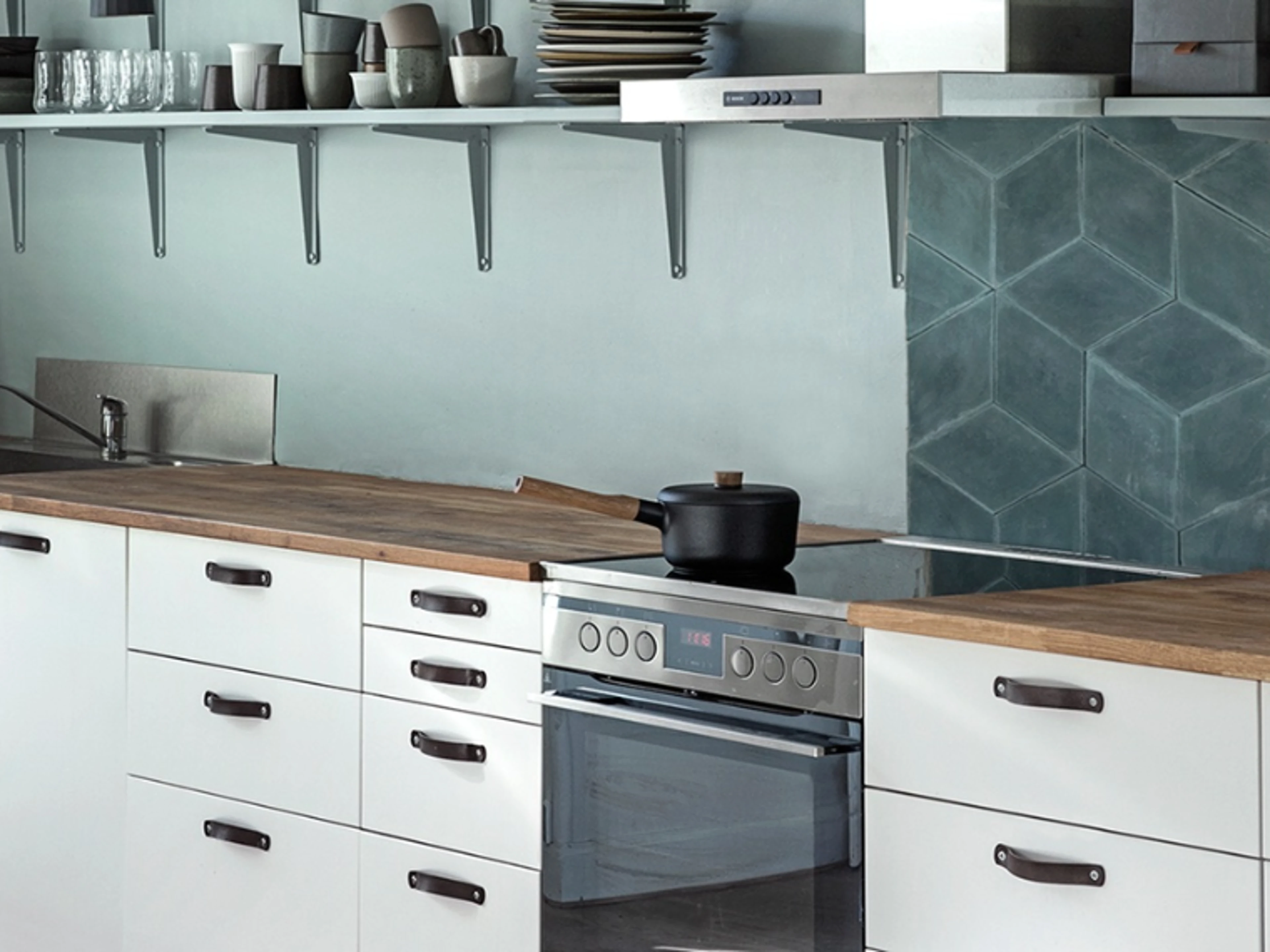 Modern kitchen with light blue walls, white cabinets, wooden worktops, open shelving and geometric blue wall tiles.