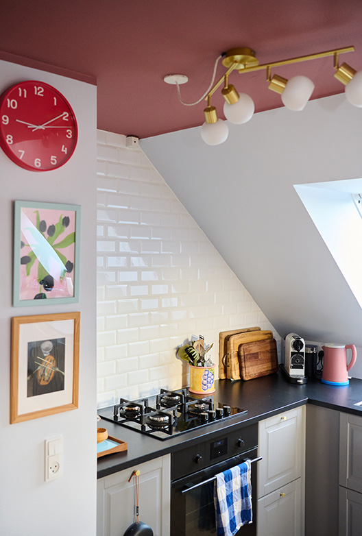 Køkken med hvide fliser og rosa loft, indrettet med komfur, træskærebrætter og farverige detaljer.
