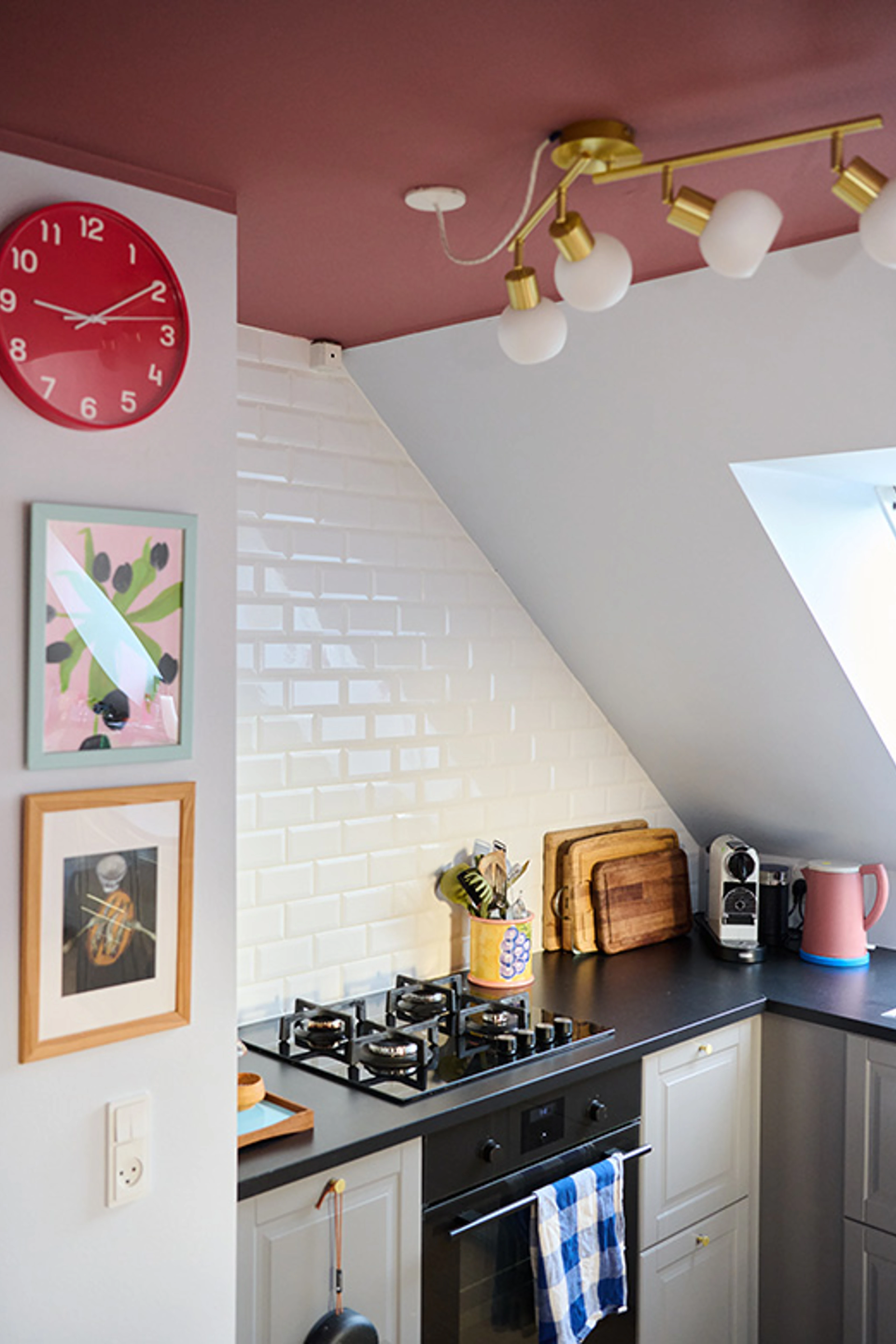 Køkken med hvide fliser og rosa loft, indrettet med komfur, træskærebrætter og farverige detaljer.