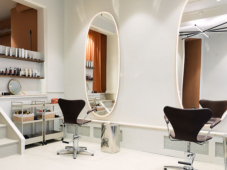 Moderne frisørsalon med frisørstole, ovale lysspejle og produktreoler.
