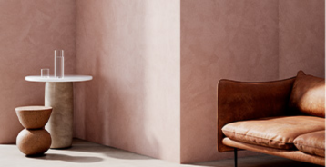 Interiør med strukturerte rosa vegger, brun skinnsofa og skulpturelle sidebord.